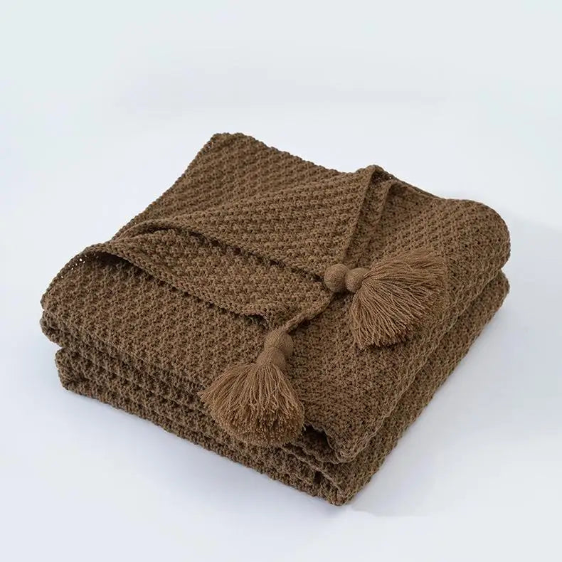 Une couverture en tricot brun avec des glands décoratifs, parfaite pour un look cocooning.