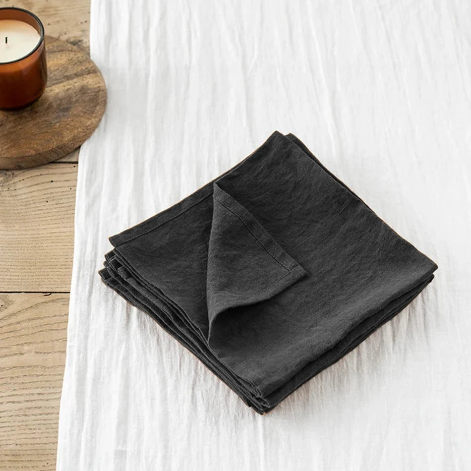 Serviettes de table noires pliées sur une surface en bois clair avec une bougie allumée à proximité, créant une atmosphère apaisante et élégante.