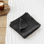 Tissu de lin noir plié sur une surface en bois avec une bougie allumée.