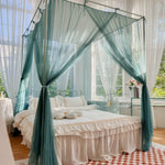 Lit à baldaquin invitant avec des rideaux translucides de couleur vert menthe dans une chambre lumineuse avec des fenêtres donnant sur un paysage verdoyant.