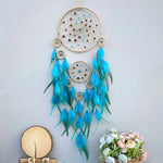Un magnifique attrape-rêves bleu et doré suspendu, décoré de plumes ondoyantes et de perles brillantes, créant une œuvre d'art naturelle et élégante.