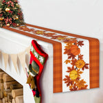 Une table recouverte d'un chemin de table décoré de feuilles d'automne colorées et d'une décoration festive au-dessus.
