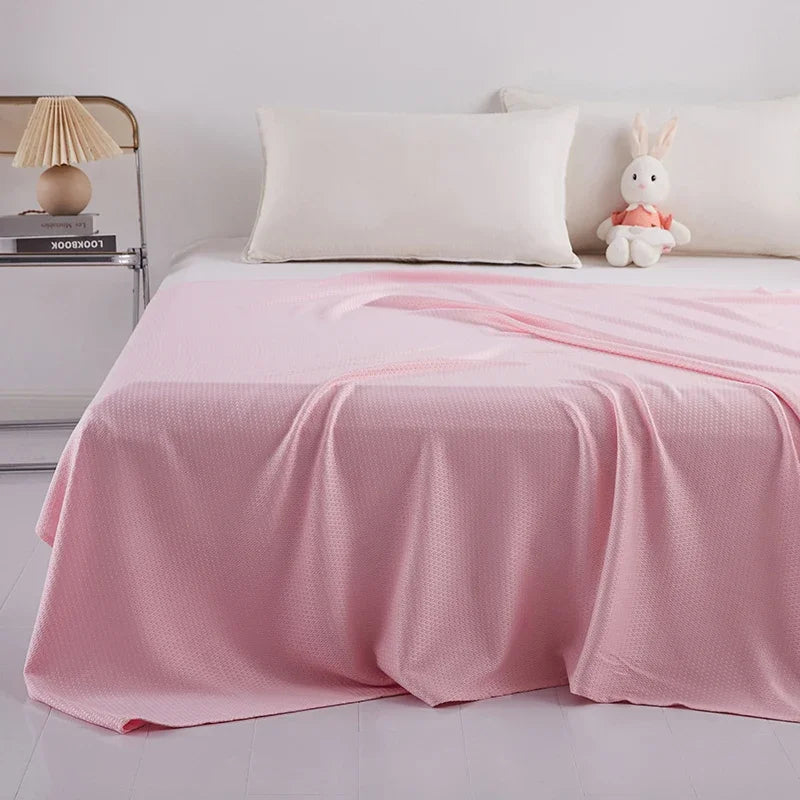 Une couverture rose pastel douillette et confortable recouvre ce lit, avec un coussin blanc et une peluche de lapin posés sur le côté, créant une ambiance reposante et accueillante.