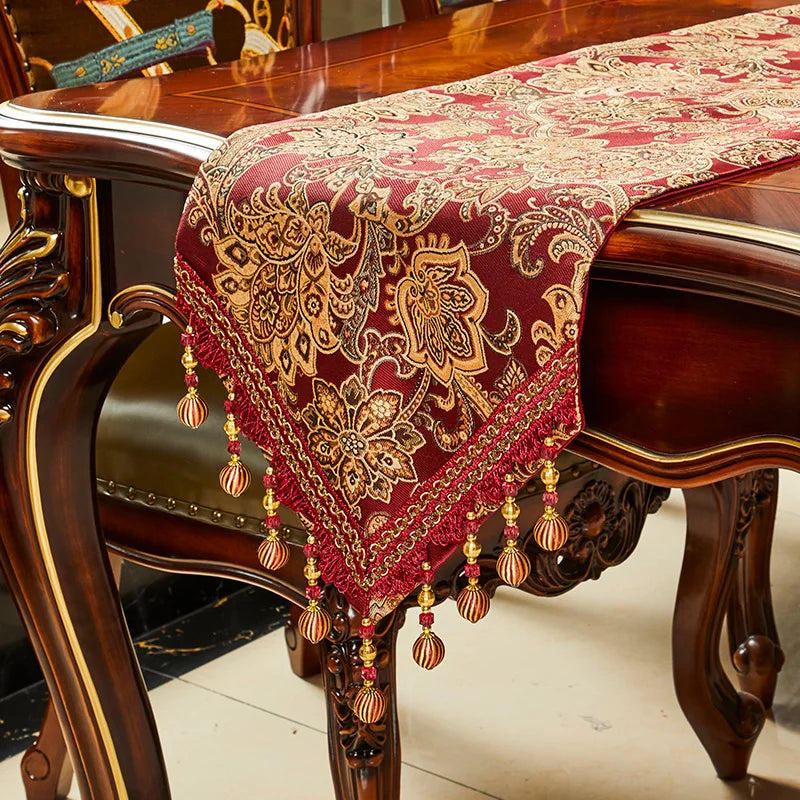 Une table de style baroque avec un magnifique chemin de table en motifs floraux dorés sur fond rouge, décoré de pompons et de perles.