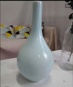 Vase en céramique de couleur vert clair, posé sur une surface blanche, entouré d'autres accessoires de décoration.
