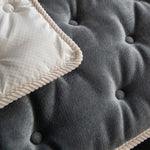 Gros plan sur un plaid gris duveteux avec une texture moelleuse et des boutons décoratifs, offrant un aspect confortable et douillet.