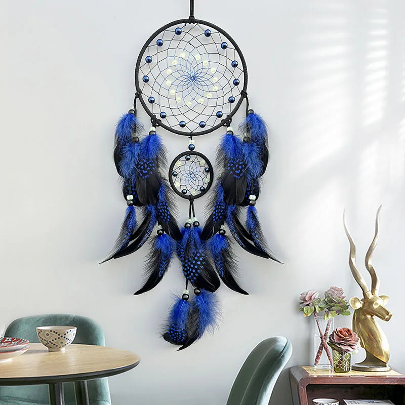 Un capteur de rêves décoratif en noir et bleu composé de plumes et de perles, suspendu au mur devant une table et des fleurs.
