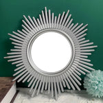 Miroir décoratif en forme de soleil couleur or accroché sur un mur blanc