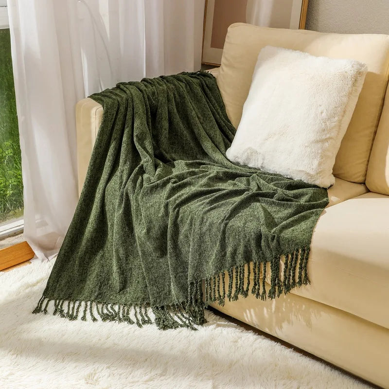 Une couverture moelleuse et texturée de couleur verte, ornée de franges, posée sur un canapé blanc dans un salon cosy.