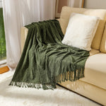 Une couverture moelleuse et texturée de couleur verte, ornée de franges, posée sur un canapé blanc dans un salon cosy.