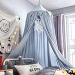 La chambre comprend un lit avec un ciel de lit gris en forme de dôme, décoré de pompons et orné de guirlandes lumineuses, créant une atmosphère apaisante et chaleureuse.