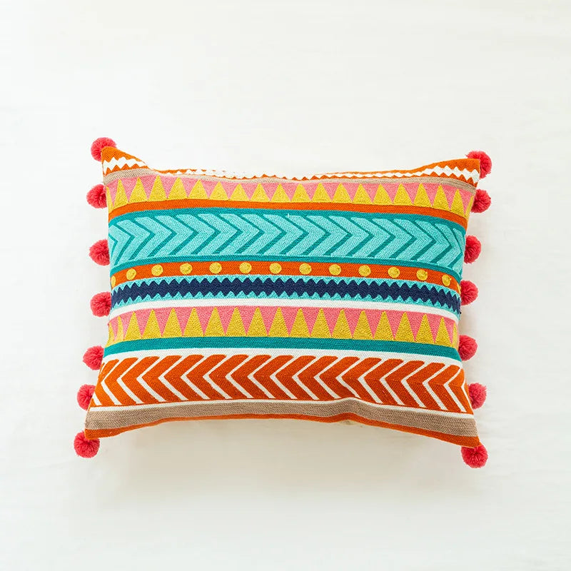 Coussin décoratif coloré avec des motifs géométriques et des pompons, offrant une touche bohème et chaleureuse à l'intérieur.