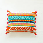 Coussin décoratif coloré avec des motifs géométriques et des pompons, offrant une touche bohème et chaleureuse à l'intérieur.