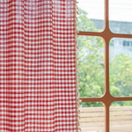 Rideau à carreaux rouges et blancs avec franges, suspendu près d'une fenêtre lumineuse. Parfait pour ajouter une touche de charme rustique à votre intérieur tout en offrant une touche de couleur vive à votre décoration.