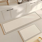 Deux tapis de cuisine rectangulaires beiges avec bordures gris foncé placés sur le sol d'une cuisine blanche moderne.