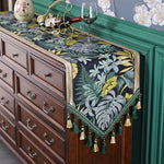Une élégante décoration murale peinte à la main ornée de motifs floraux tropicaux sur fond sombre, posée sur une belle commode en bois sombre avec des ustensiles de vin.