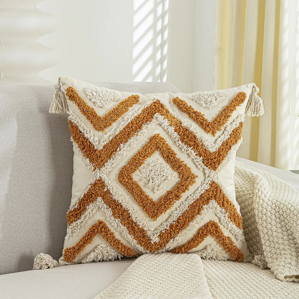 Coussin décoratif à motifs géométriques dans des tons ocre et beige, avec des franges.