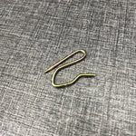 Un crochet à rideau en métal doré posé sur une surface grise texturée.