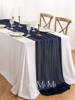 Une table élégante avec une nappe blanche et un chemin de table bleu marine, ornée de chandeliers et de verres de cristal, créant une ambiance chic et raffinée.