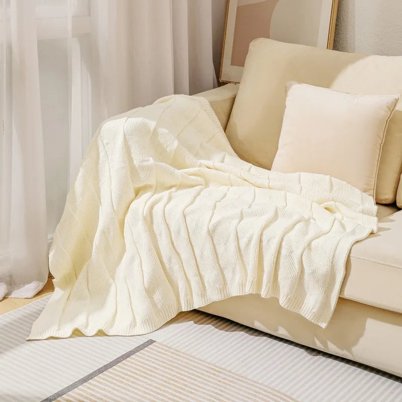 Une couverture en tricot blanc décorant un canapé confortable dans un intérieur chaleureux et élégant.