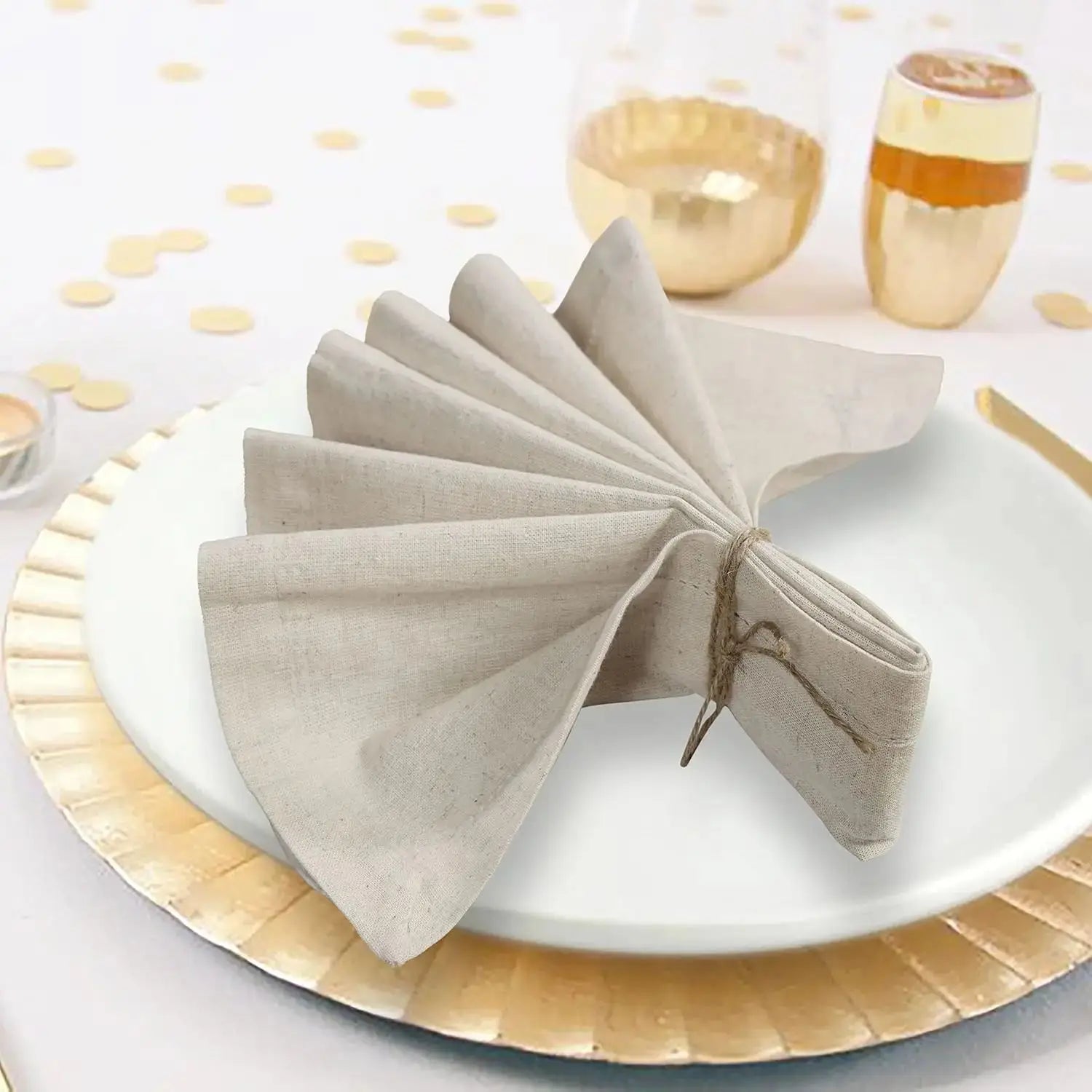 Sur un plateau blanc se trouve un raffiné pliage de serviette de table grise, entouré d'un linge doré et de bols de céramique dorée, créant une ambiance chaleureuse et élégante.