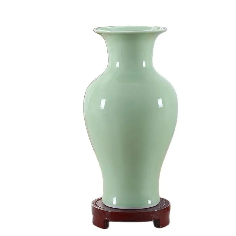 Ce vase en céramique lisse de couleur vert pastel est posé sur un socle en bois foncé, créant un contraste élégant et équilibré.