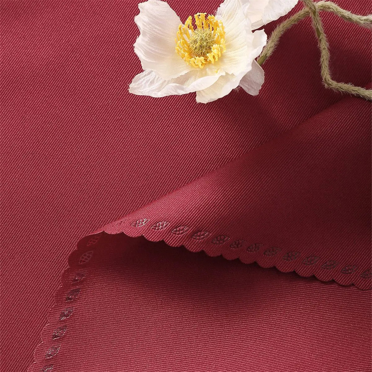 Fleur blanche élégante posée sur un fond soyeux rouge foncé avec des motifs délicats.