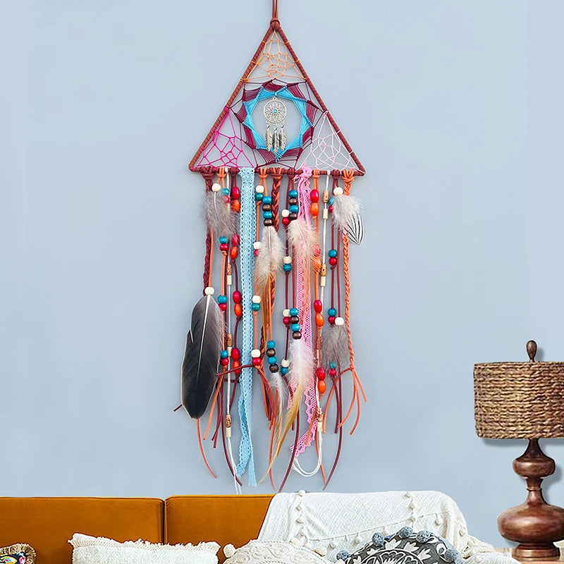 Un magnifique attrape-rêves triangulaire coloré, suspendu au mur, décoré de plumes, de perles et d'un capteur de rêves en son centre, apportant une touche de bohème et de spiritualité à l'espace.