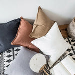 Cette image dépeint un arrangement de coussins décoratifs dans des tons de blanc, beige et noir, posés sur un tapis motif géométrique. L'ensemble crée une atmosphère chaleureuse et confortable dans un intérieur.