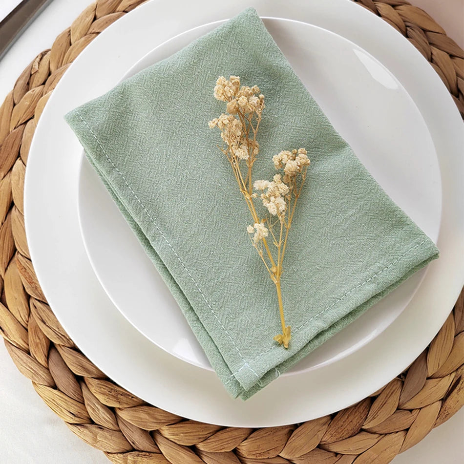 Linge de table vert olive avec un joli bouquet de fleurs séchées sur une assiette blanche posée sur un dessous de plat en paille.