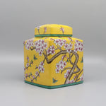 Ce pot de stockage en céramique jaune est orné de motifs floraux roses et de papillons, créant une impression de nature printanière.