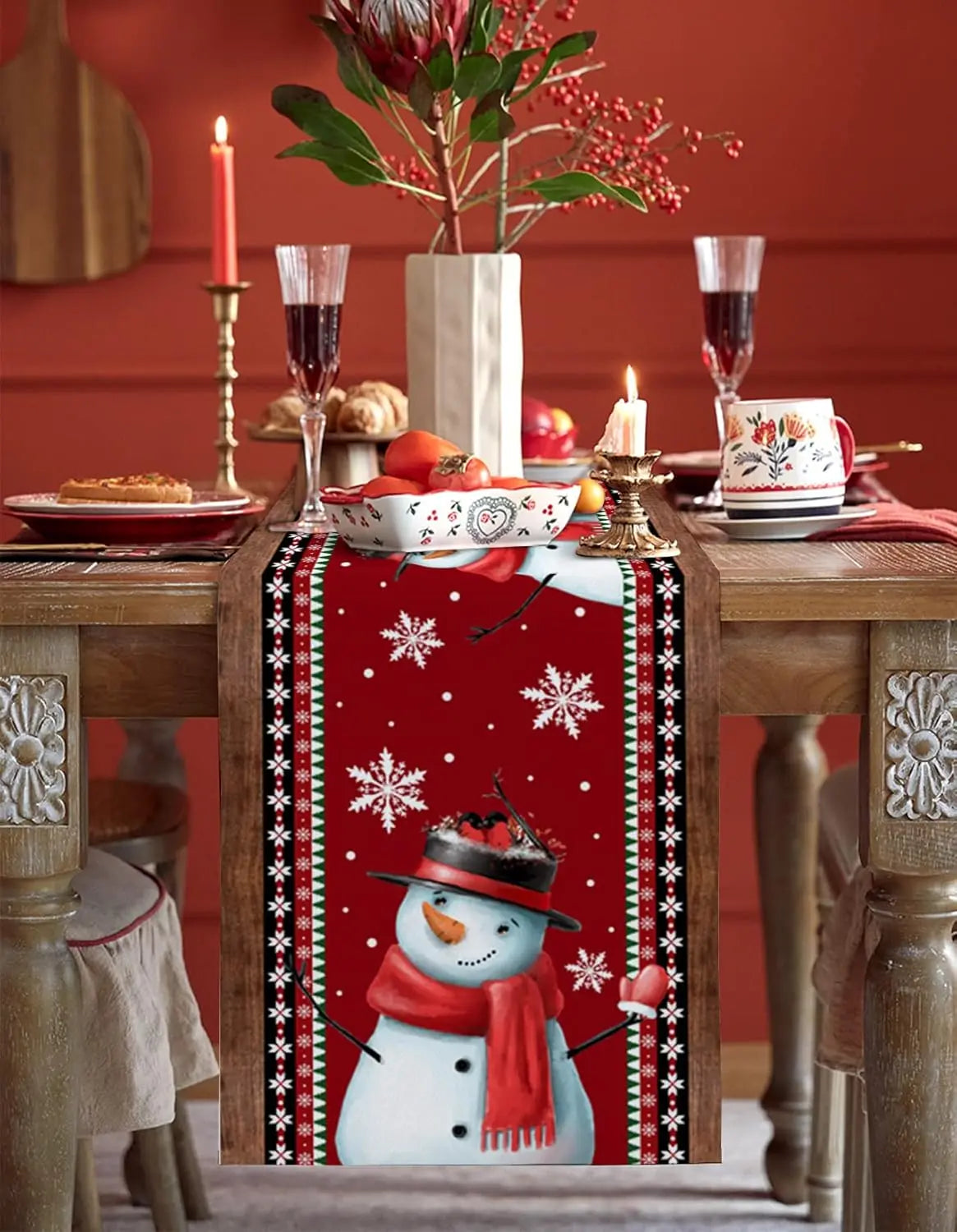 Table de Noël festive avec décorations en rouge et blanc, bougies allumées, coupes de vin et fleurs rouges dans un vase.