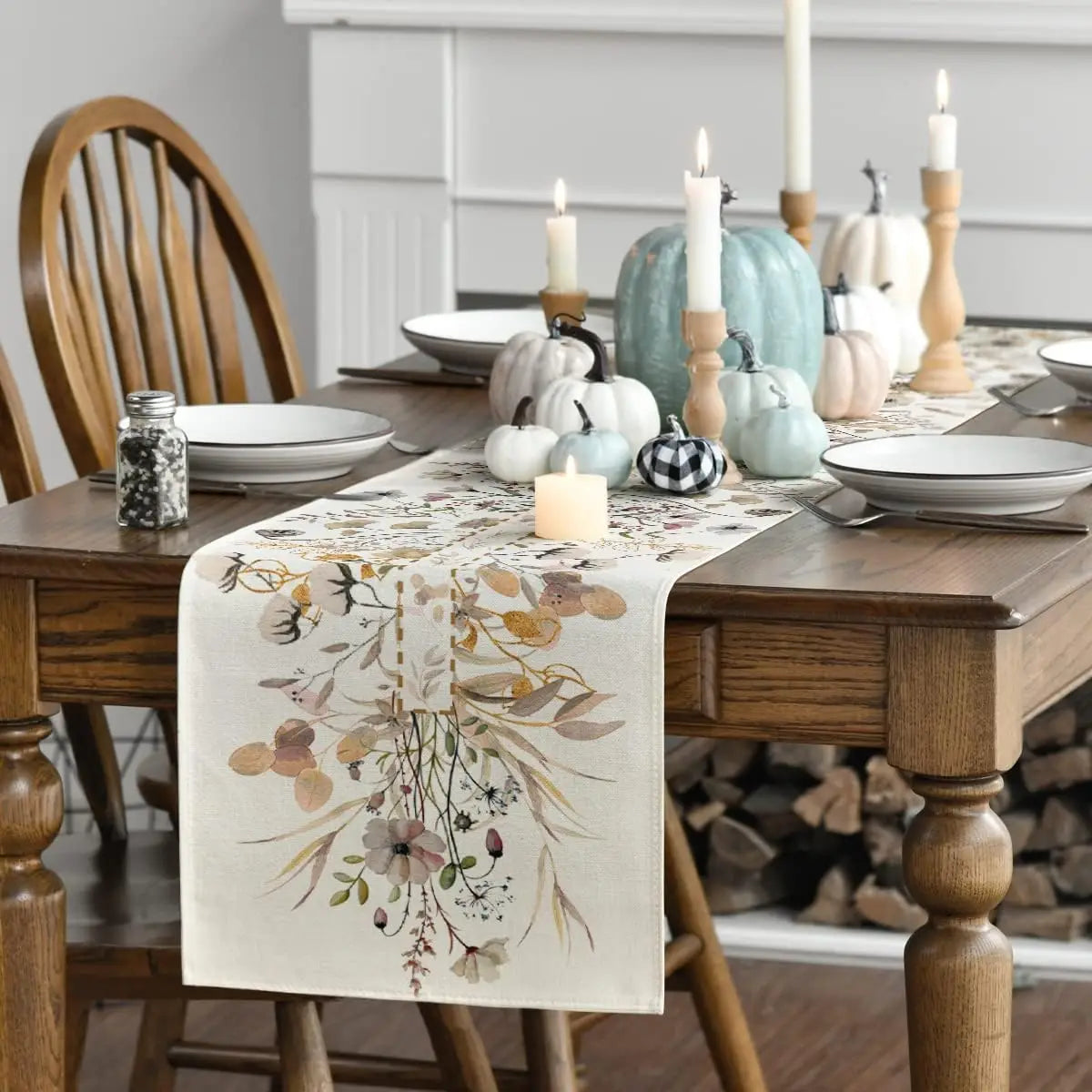 Sur une table en bois, un délicat chemin de table orné de fleurs et de motifs naturels, entouré de bougies allumées et de décorations automnales dans des tons doux.