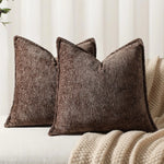 Trois coussins confortables en velours brun foncé, avec des motifs texturés, reposent sur une couverture beige moelleuse, créant une atmosphère chaleureuse et accueillante dans l'espace.