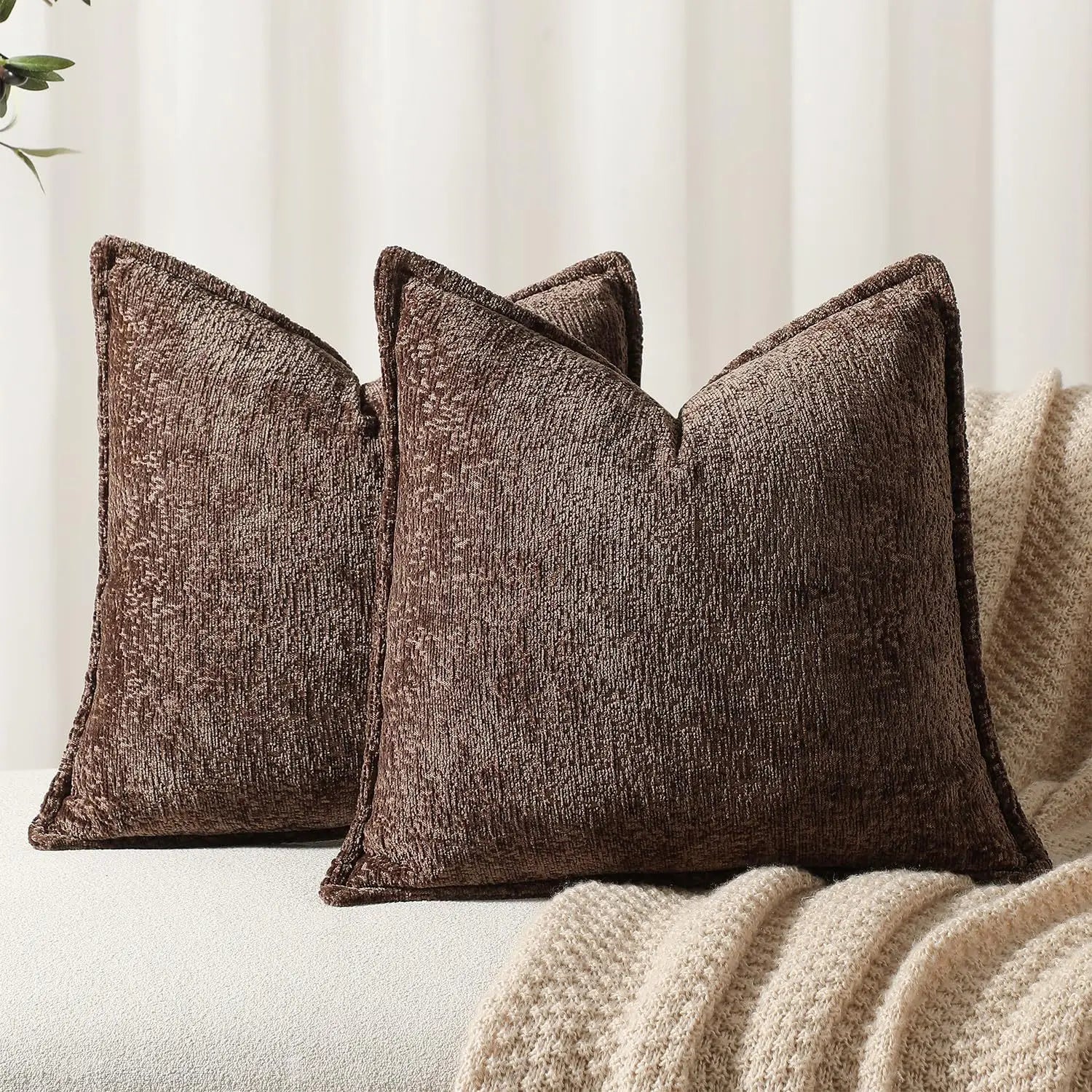 Trois coussins confortables en velours brun foncé, avec des motifs texturés, reposent sur une couverture beige moelleuse, créant une atmosphère chaleureuse et accueillante dans l'espace.