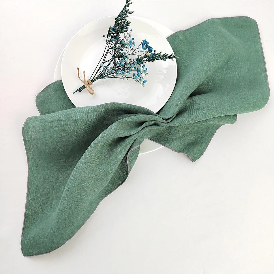 Cette image présente un élégant arrangement composé d'une assiette blanche ornée de fleurs bleues disposées avec soin, sur un fond vert pâle drapé d'un tissu aux plis gracieux.