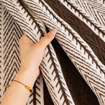 Une couverture ou un tapis tissé à motifs géométriques en blanc et marron, avec une main tenant un coin du tissu.