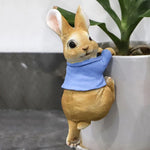 Lapin doré mignon avec un bandana bleu autour du cou, posé près d'une plante en pot.