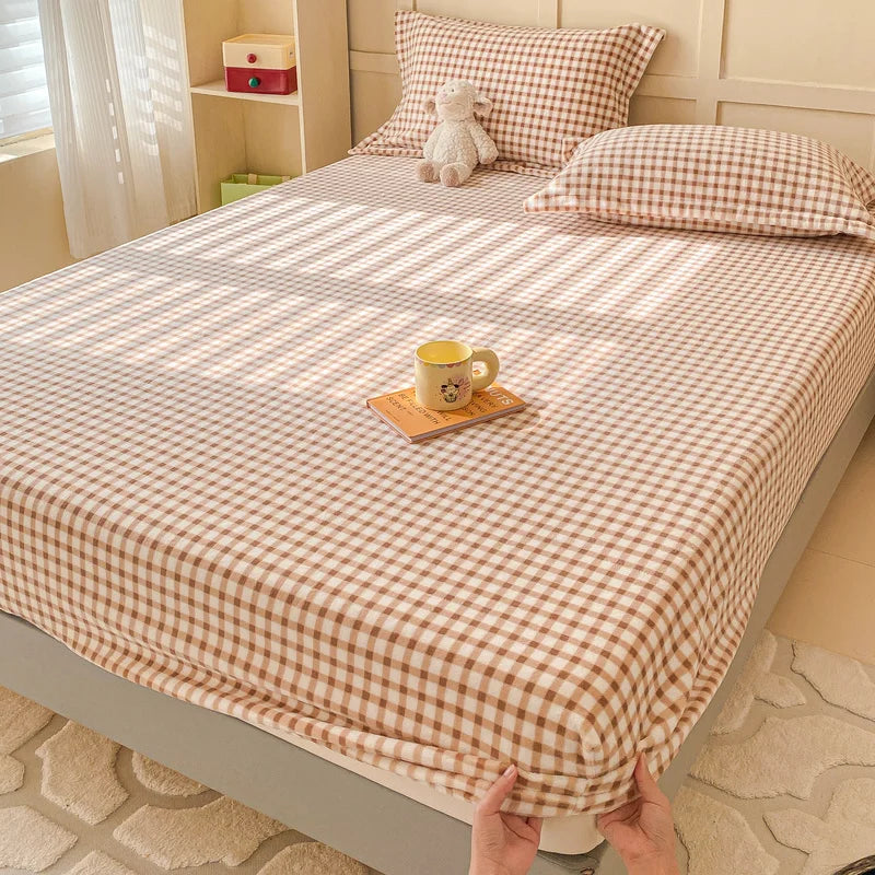 Une chambre confortable avec un lit douillet recouvert d'un édredon à motifs à carreaux beige et blanc, accompagné d'une tasse de boisson posée sur un plateau en bois.