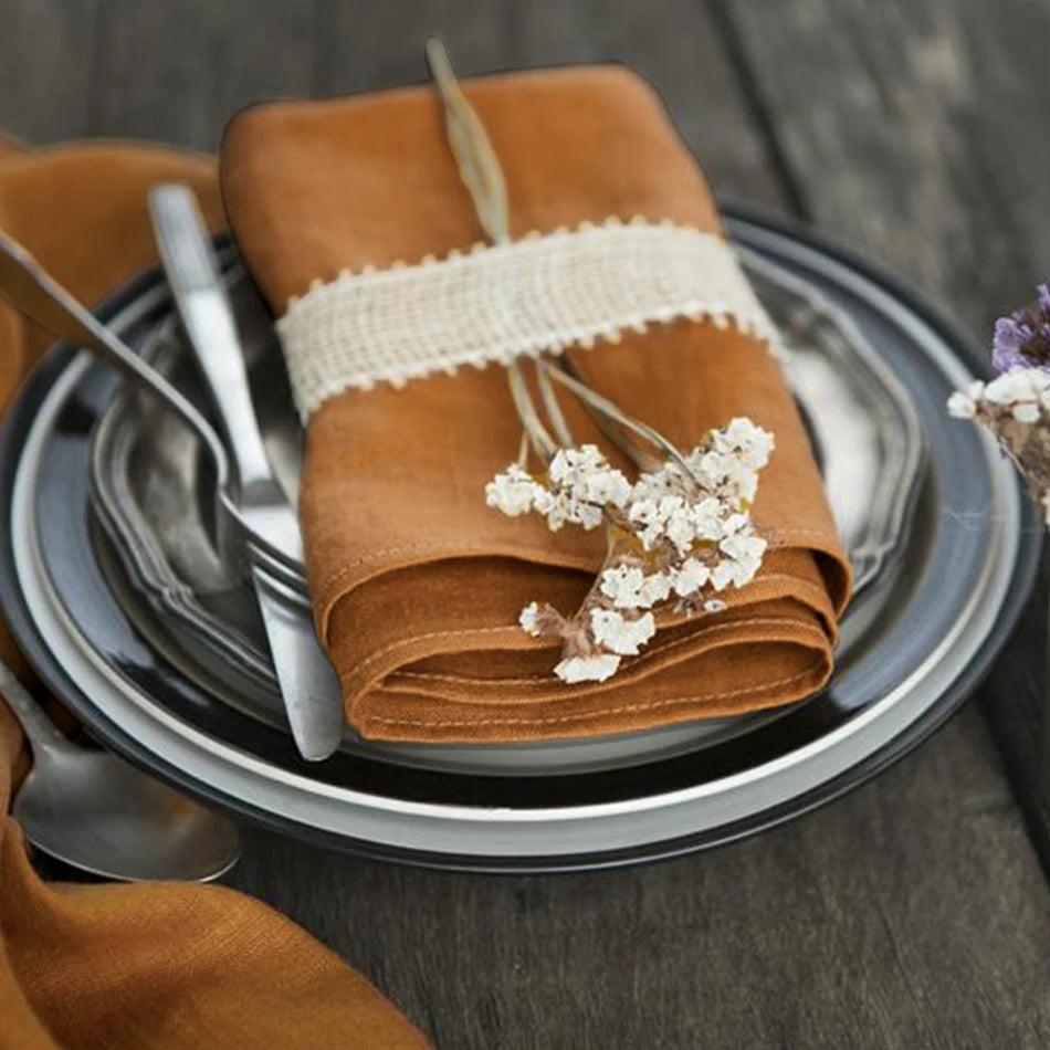 Élégant ensemble de table avec serviette en tissu beige, décorée de petites fleurs blanches, posée sur une assiette noire et grise.