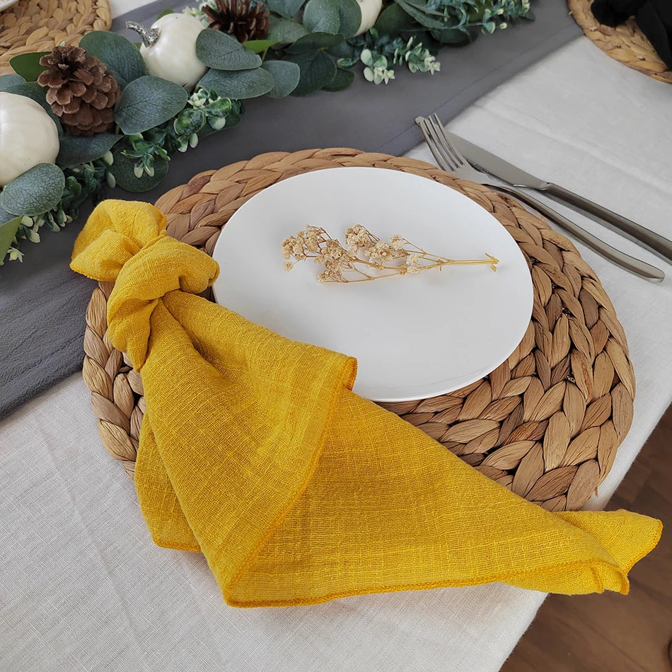 Table de cuisine décorée avec une nappe en lin jaune, un plateau en fibres tressées, des couverts et un plat en céramique blanche orné d'un élément doré.