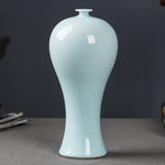 Un vase délicat et élégant en céramique de couleur vert clair, avec une forme galbée et un col étroit.