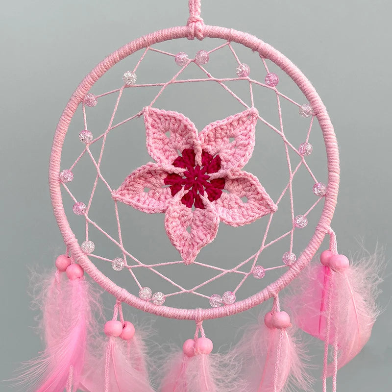 Un attrapeur de rêves rose en forme de fleur ornée de perles et de franges, suspendu dans un cadre circulaire.