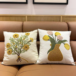 Deux coussins décoratifs blancs avec des motifs de fleurs jaunes et vertes placés sur un canapé beige.