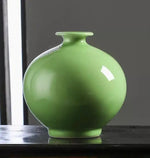 Un beau vase en céramique vert émeraude posé sur une surface sombre.