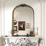 Miroir décoratif avec un magnifique cadre orné de roses et de feuillages, surmonté d'une frise florale, exposant une photographie encadrée sur une console blanche sculptée.