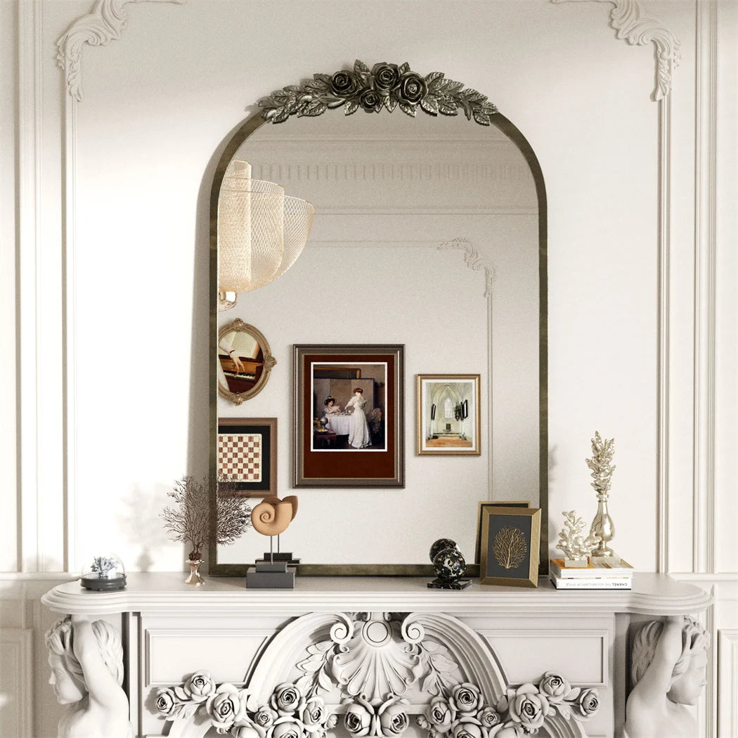 Miroir décoratif avec un magnifique cadre orné de roses et de feuillages, surmonté d'une frise florale, exposant une photographie encadrée sur une console blanche sculptée.