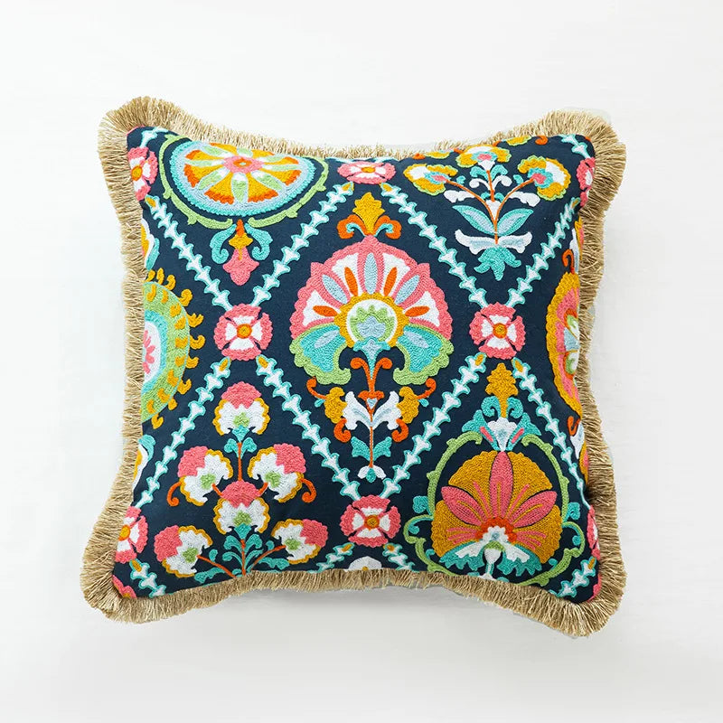 Coussin décoratif aux motifs floraux colorés et ornementés sur un fond bleu foncé, avec des franges sur les bords.