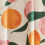 Rideau de douche orné de motifs de fruits oranges stylisés et de formes roses, sur un fond blanc, agrémenté de grandes feuilles vert foncé. 