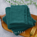 Serviettes de table en coton vert foncé sur un plateau en bois, avec des couverts métalliques à proximité.